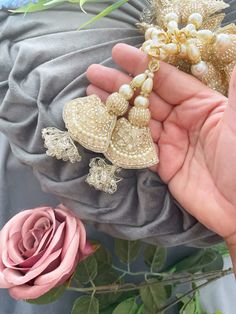 a person holding two pieces of jewelry next to a pink rose on a gray cloth