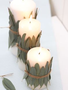 three white candles with green leaves and twine around them on a blue table cloth