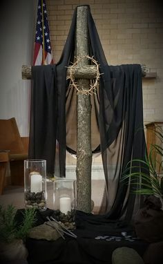 the cross is adorned with a crown and surrounded by candles, rocks, and plants