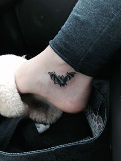 a small black bat tattoo on the foot of a person in a car with a teddy bear