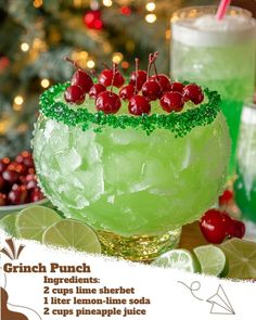 a green drink with cherries and limes on the rim next to a christmas tree