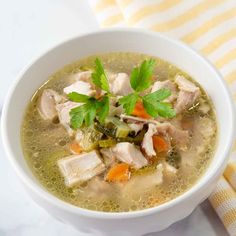 a white bowl filled with chicken soup and garnished with cilantro leaves