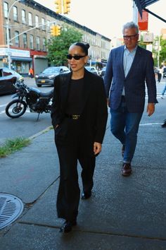 a woman walking down the street with a man wearing a suit and tie behind her