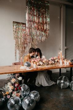 a bride and groom sitting at a table surrounded by disco balls, candles and flowers