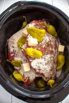 a slow cooker filled with meat covered in cheese and jalapeno peppers