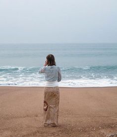 a woman standing on top of a sandy beach next to the ocean