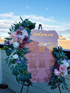 a pink sign with flowers and greenery on it