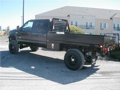 a black truck is parked in front of a building with large tires on it's flatbed