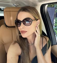 a woman sitting in the back seat of a car talking on a cell phone while wearing sunglasses