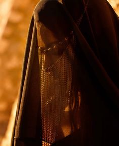 a person wearing a veil and glasses in front of a stone wall with sunlight streaming through it