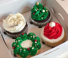 four decorated cupcakes in a box with white frosting and green icing