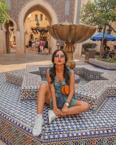 a woman sitting on top of a blue and white bench next to a water fountain