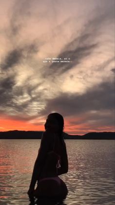 a woman is sitting in the water at sunset