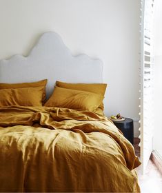 a bed with yellow sheets and pillows in a white room next to an open window