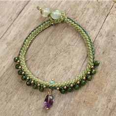 a green bracelet with a purple bead and an amethoraite charm on it