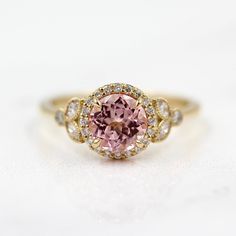 a fancy ring with a pink stone surrounded by white and yellow diamonds on a white background