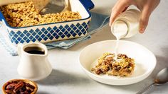 a person pouring milk into a bowl filled with granola and other food on a table