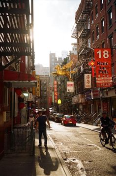 a man walking down a street next to tall buildings and cars on the side walk