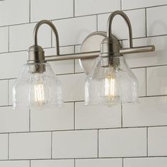 two light bathroom fixture with clear glass shades on white tile wall behind brick patterned backsplash