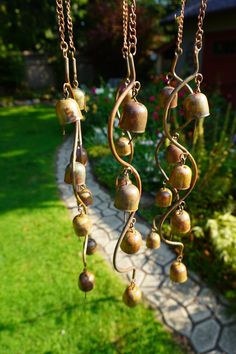 three bells hanging from a chain in the grass near a path and flowerbeds