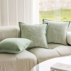 two green pillows sitting on top of a white couch next to a glass coffee table