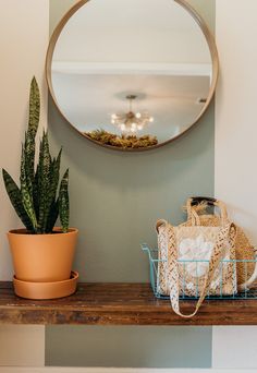 a round mirror hanging on the wall above a shelf next to a potted plant