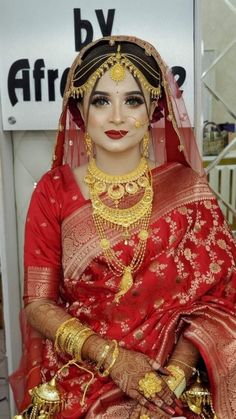 a woman in a red and gold bridal outfit with jewelry on her head, sitting down