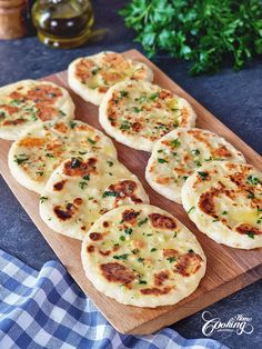 several flat breads with cheese and parsley on a cutting board next to some herbs