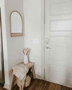 a white vase sitting on top of a wooden bench in front of a door with a mirror above it