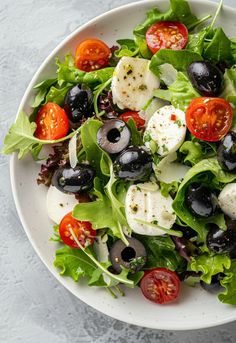 a salad with mozzarella, olives, tomatoes and lettuce in a white bowl