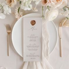 a table setting with white flowers and silverware on the plate, along with menu cards