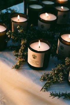 many candles are lit on a table with greenery