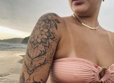 a woman with tattoos on her arm and chest standing next to the ocean in front of an overcast sky