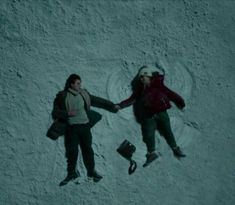 two people laying in the snow next to each other and one person holding a suitcase