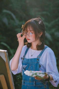 a young woman holding a brush to her eye while standing next to an easel