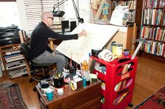 a man sitting at a desk with lots of art supplies on top of his desk