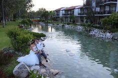 a bride and groom are sitting on rocks by the water in front of their apartment buildings