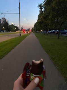 someone holding up a piece of chocolate in the middle of a road with cars parked on both sides