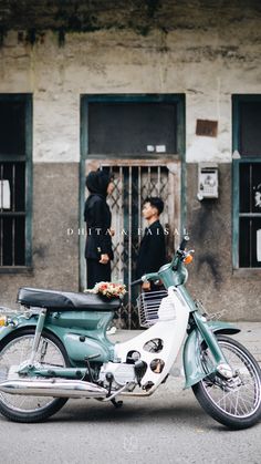 a motorcycle parked in front of a building with two people standing behind it on the sidewalk