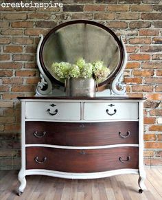 an old dresser with flowers on it and a round mirror above the top, in front of a brick wall