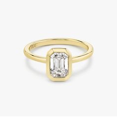 a yellow gold ring with an emerald cut diamond in the center, on a white background