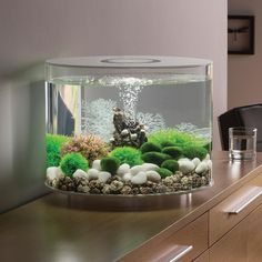 a fish tank filled with water and rocks on top of a wooden table next to a window