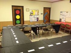 an empty classroom with tables and chairs covered in black tablecloths, next to bulletin boards on the wall