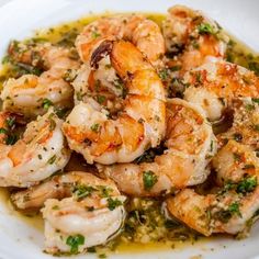 a white plate topped with cooked shrimp covered in sauce and garnished with parsley