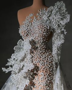 the back of a wedding dress with white and silver flowers on it's shoulders