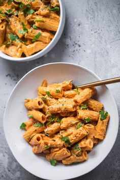 two white bowls filled with pasta and garnished with parsley on the side