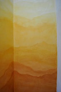 an orange and yellow painting with mountains in the backgroung, on a white wall