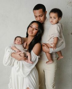 a man and woman holding two babys in front of a white wall with the caption's name on it