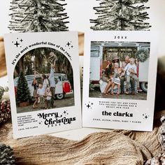 two christmas cards sitting on top of a table next to pine cones and fir trees