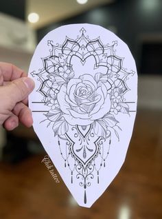 a hand holding up a paper cutout with a rose on the front and an ornate design on the back